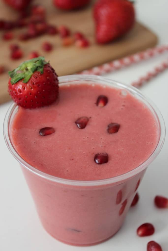 Pomegranate Strawberry Smoothie with a sliced strawberry and pomegranate seeds on top.