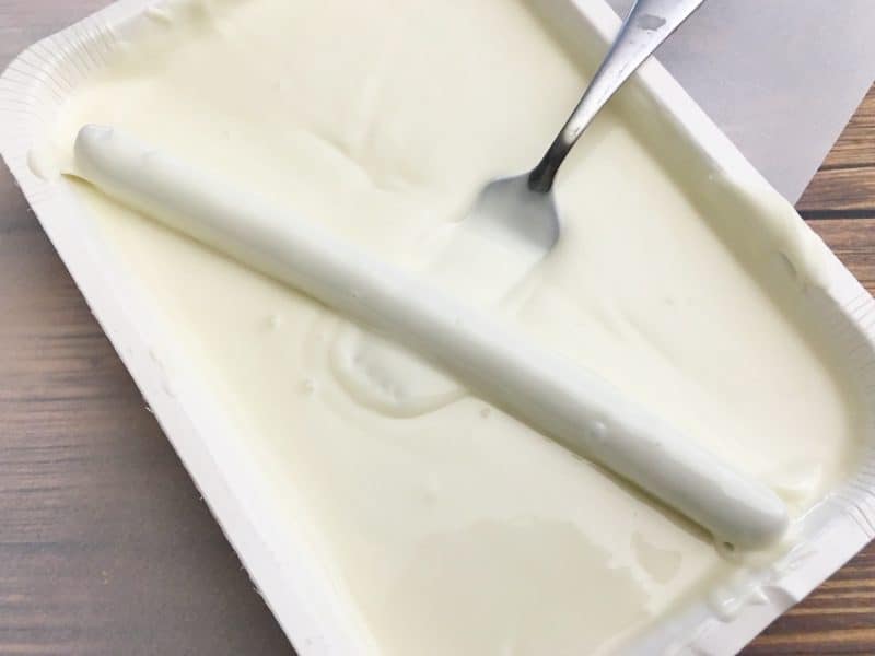 Dipping pretzel rods in melted white chocolate with a fork. 