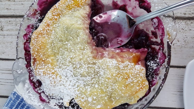 Rustic Blueberry Tart with a spoon on a white background made with fresh blueberries for a simple blueberry tart. 