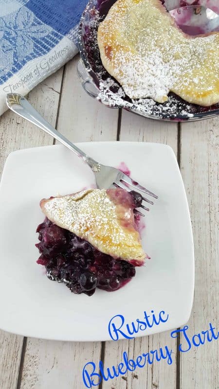 Rustic Blueberry Tart made with puff pastry and flesh blueberries on a white plate with a fork.