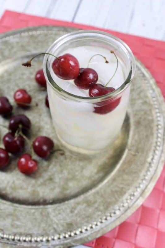 Cherry Sangria in a glass topped with fresh cherries on a silver platter. 