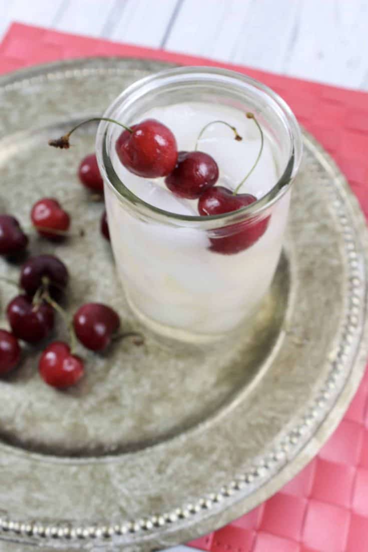 Cherry Sangria in a glass topped with fresh cherries on a silver platter.