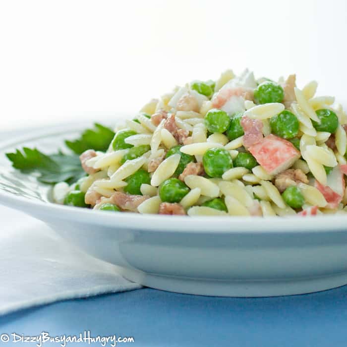 intimation crab, orzo pasta, peas and bacon combined to make a crab pasta salad in a serving bowl