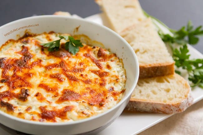 a cheesy hot crab dip made with imitation crab with a side of bread in a serving bowl