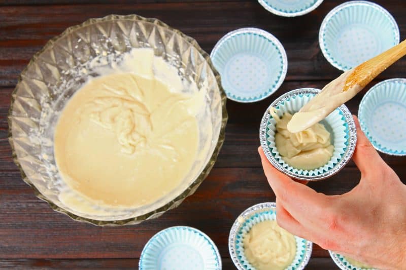 Vanilla cupcake batter being dished into cupcake liners.