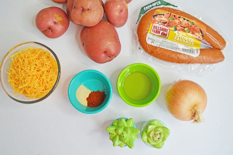 Ingredients on a countertop. Sausage and potatoes with oil, seasonings, shredded cheese and an onion