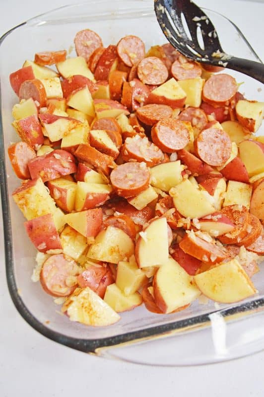 Sausage and potatoes with diced onions in a clear baking dish