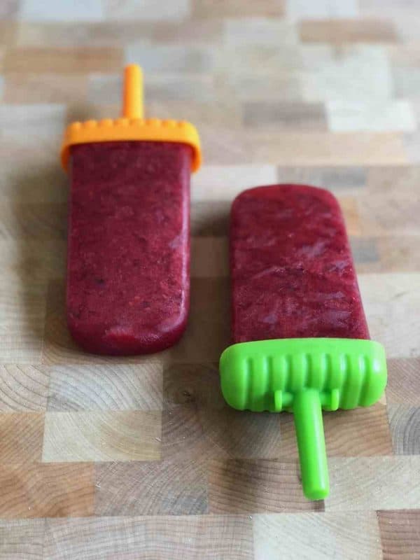 Frozen mint berry popsicles laying against a wood background. 