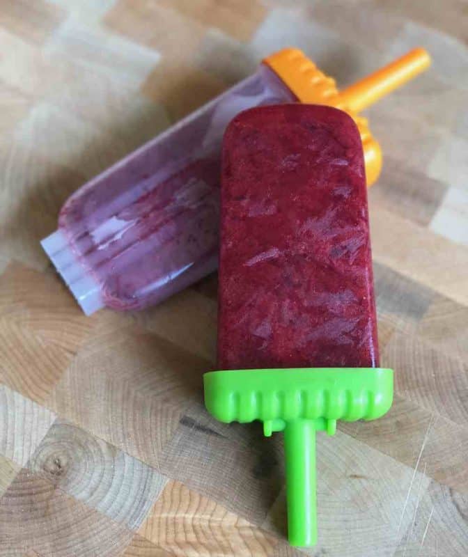 Frozen mint berry popsicles laying against a wood background. 