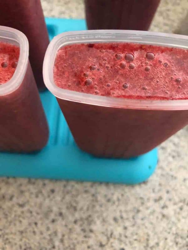 Mint berry popsicle puree being poured into popsicle molds. 