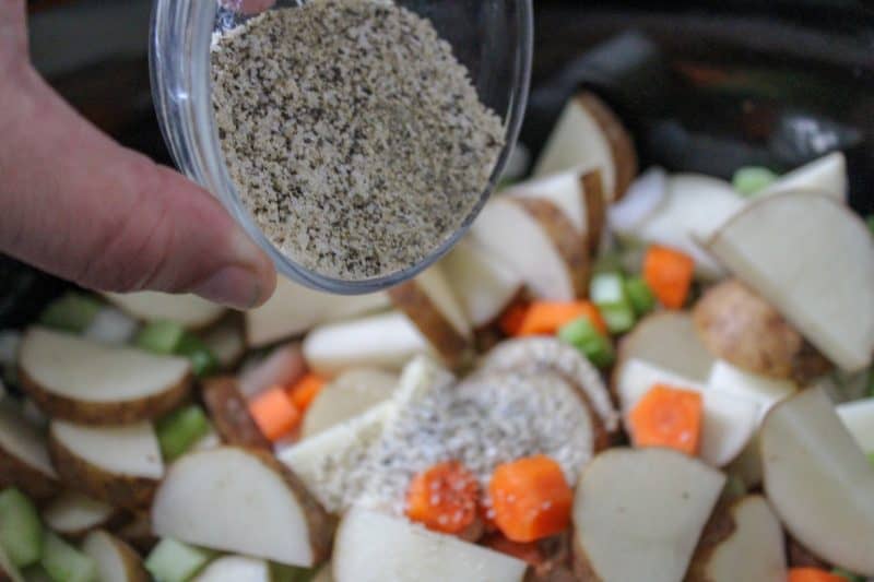 Pouring in a mixture of seasonings for a beef stew recipe. 