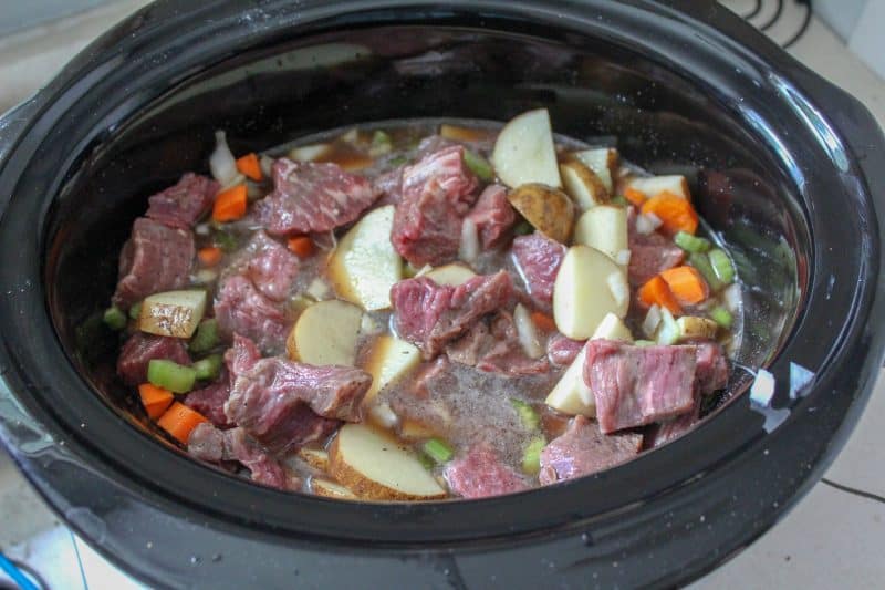 Diced meat and vegetables in a slow cooker for a homemade beef stew recipe. 