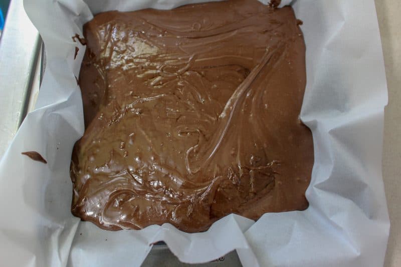 Easy fudge recipe being poured into a pan with parchment paper. 