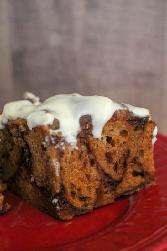 Crockpot cinnamon roll casserole on a red plate with icing dripping down the side. 