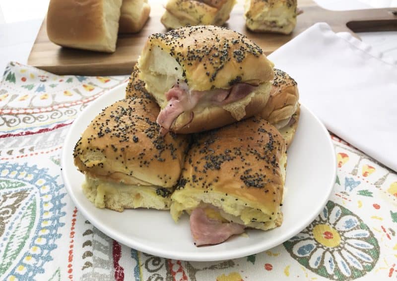 Ham and swiss cheese sliders stacked on a white plate. 